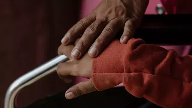 Hands resting together near wheelchair handle