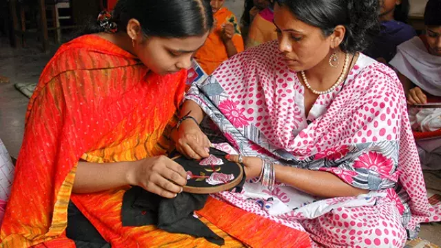 Two women sitting together and focusing on embroidery work.