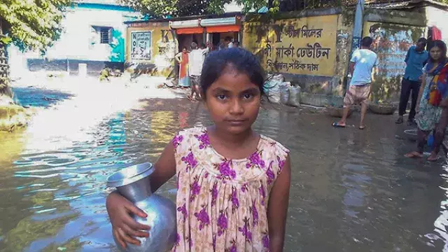 A girl holding a bowl in a flooded village.