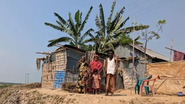 A family standing outside their corrugated metal home with a banana tree behind them.