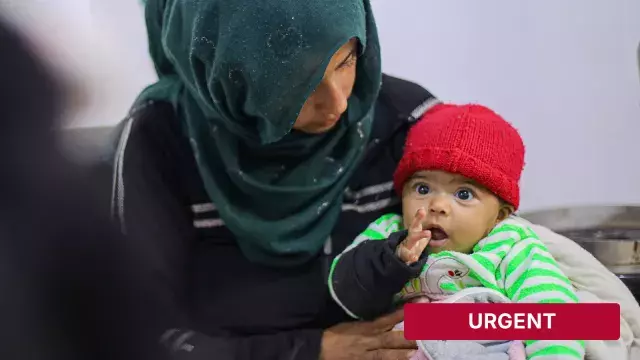 Adult holding baby in red hat with urgent label