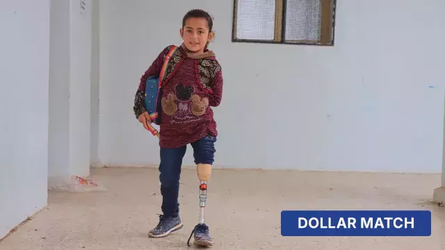 Child with prosthetic leg walking indoors with dollar match label