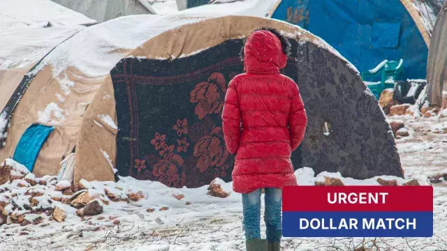 Person in red coat near snowy tents with urgent sign